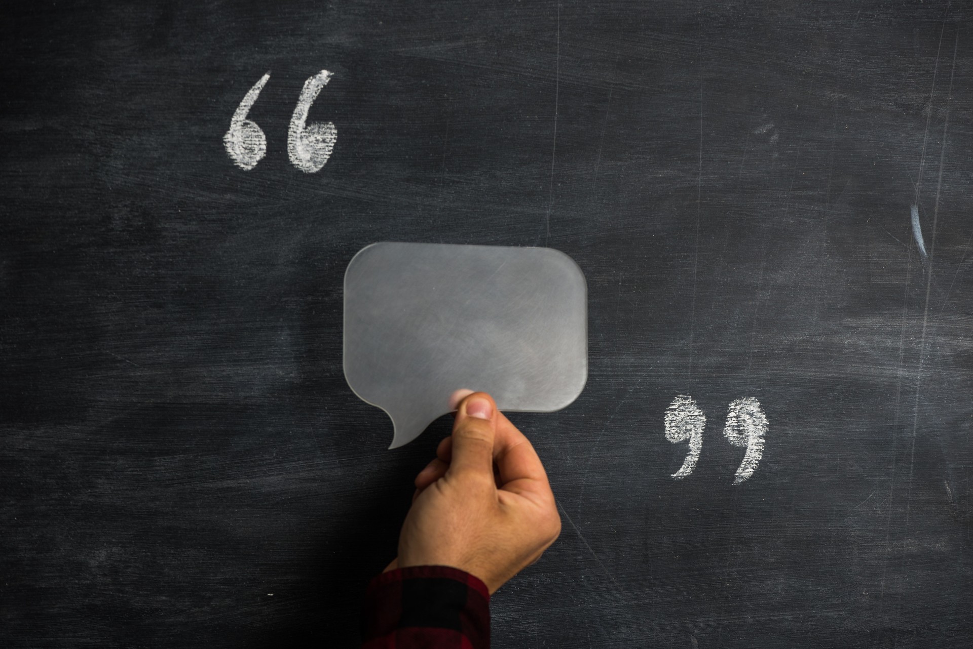 Man holding speech bubble between quotation marks on blackboard